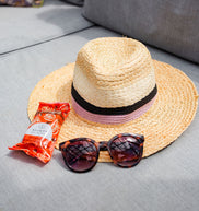 Straw hat with sunglasses and a snack on a gray surface