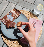 Person holding a chocolate bar over a plate with a glass of water and lemon on a wooden table.
