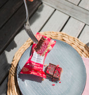 Person holding a fork over a plate with a RaspBounty chocolate bar on a wooden surface
