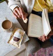 Person reading a book with a cup of coffee and a packet of vanilla bites