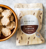 Packaged vanilla coconut bites with a bowl of bites on a marble surface