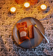 Candlelit table setting with a plate of food and cutlery on a patterned tablecloth.