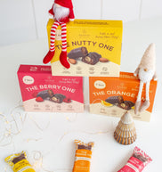 Assorted snack bars with packaging on a white surface, featuring a small elf figure.