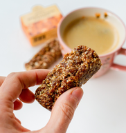 Hand holding a flapjack bar with a cup of coffee 