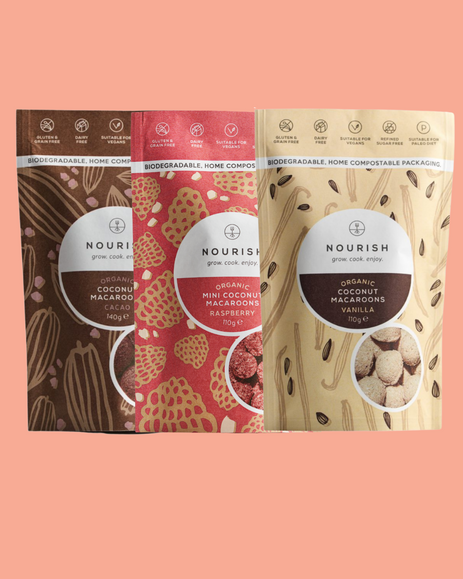 Three packages of Nourish coconut macaroons on a pink background